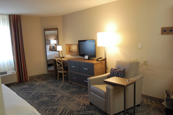 A hotel room with a bed, a desk with a computer, a chair, a television, and a lamp.