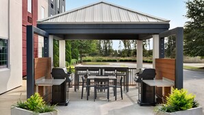 An outdoor patio with a covered seating area, grill stations, and planters.