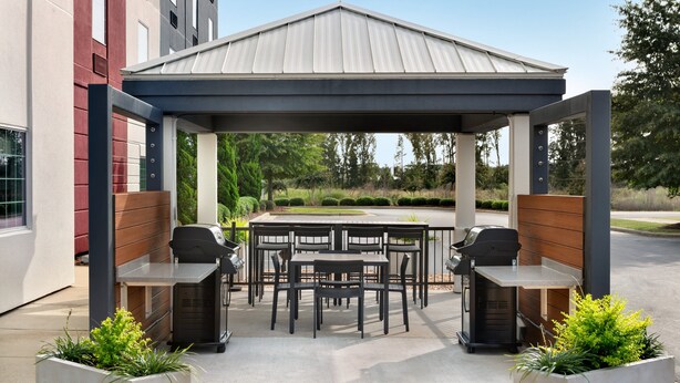 Un patio al aire libre con zona de estar techada, estaciones de parrillada y jardineras.