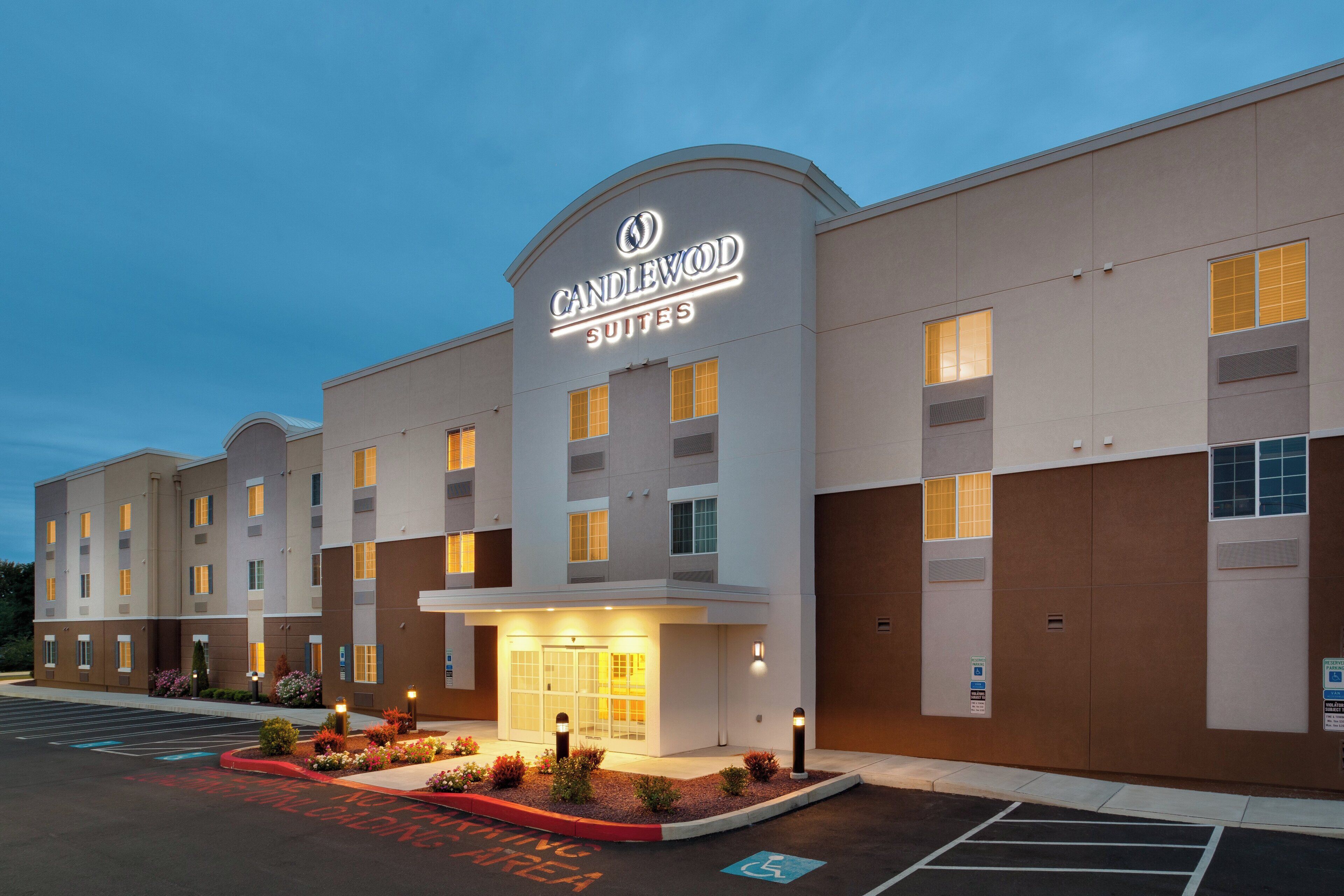 A hotel with a prominent 'Candlewood Suites' sign, a parking area with marked handicapped spaces, and a well-lit entrance.