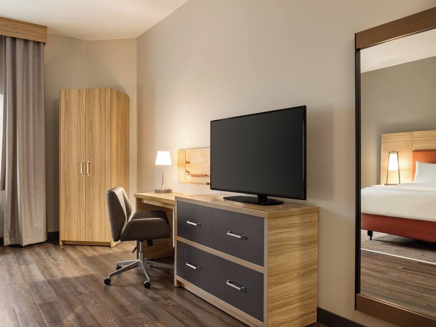 A hotel room with a wooden desk, a television, a chair, a bed, and a large mirror.