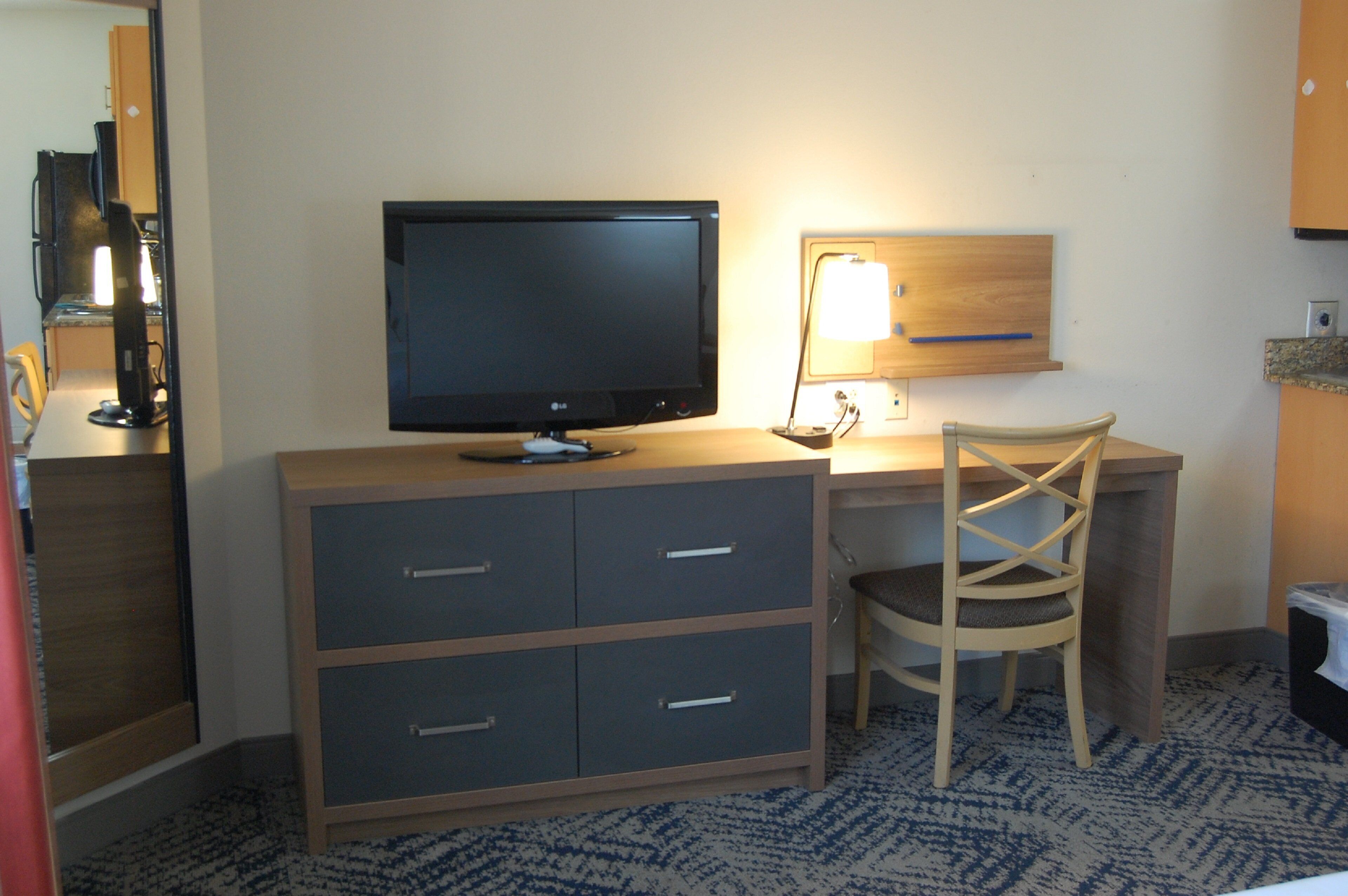 A hotel room with a desk, a chair, a television, and a lamp.