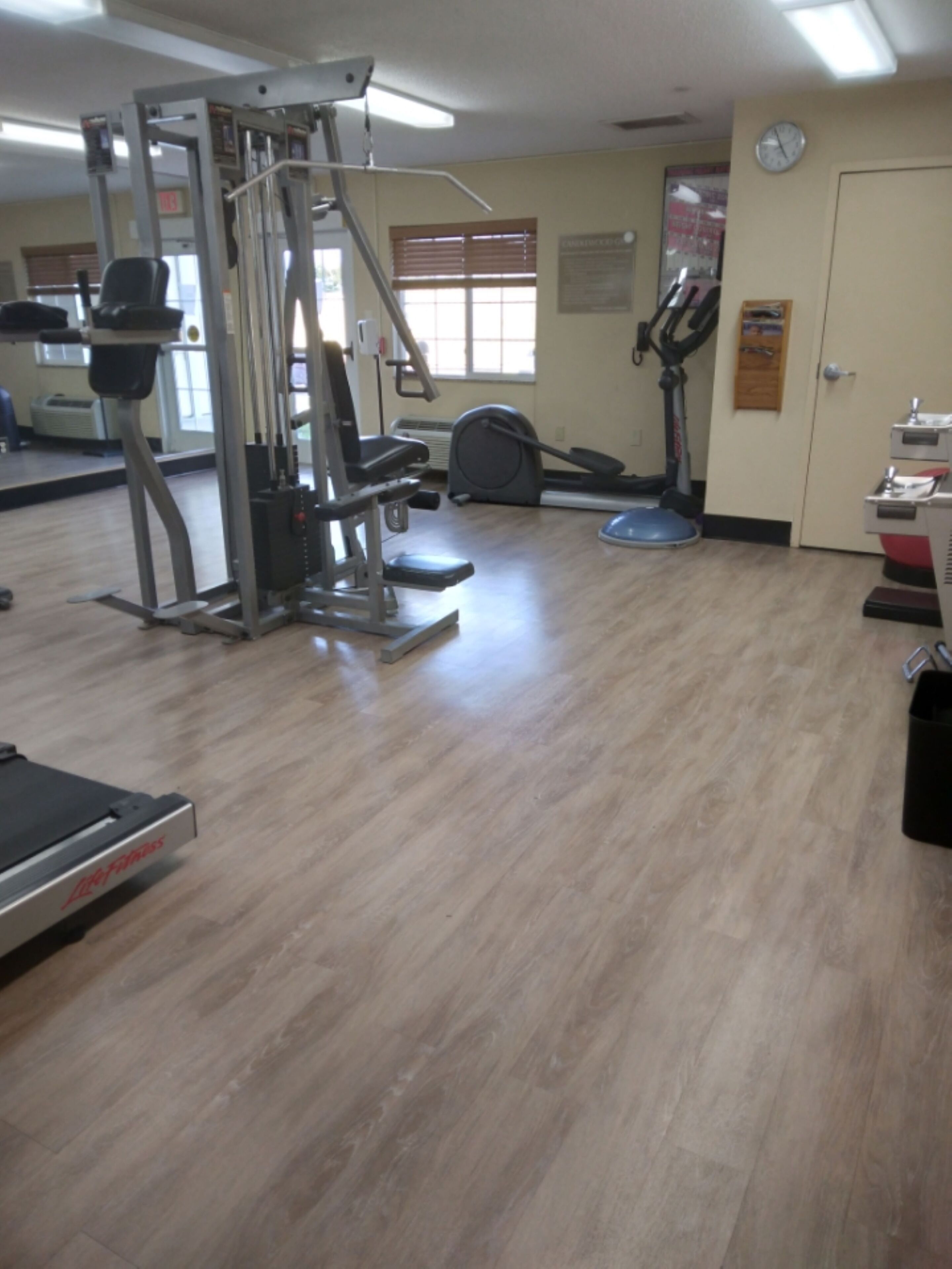 A gym with exercise equipment, a clock on the wall, and a window with blinds.
