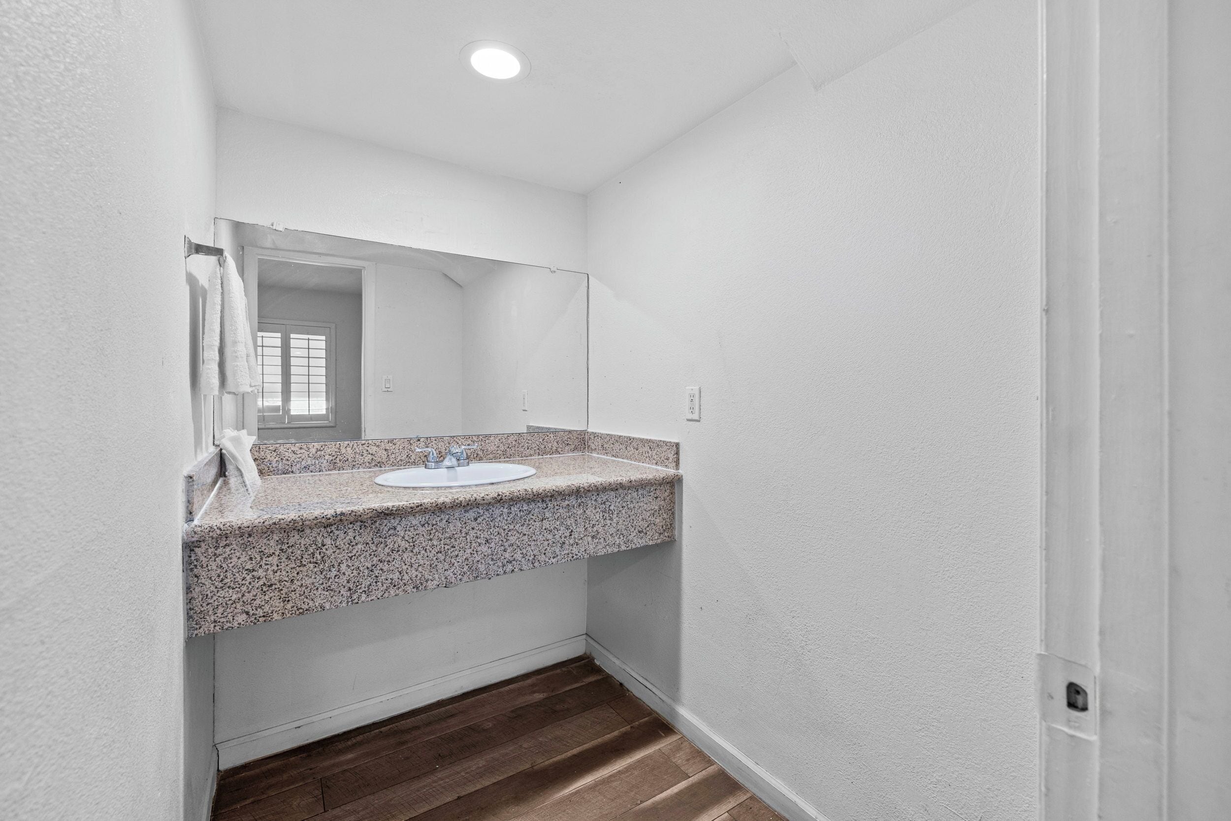 Un baño con lavamanos de encimera de granito, espejo y suelo de madera.