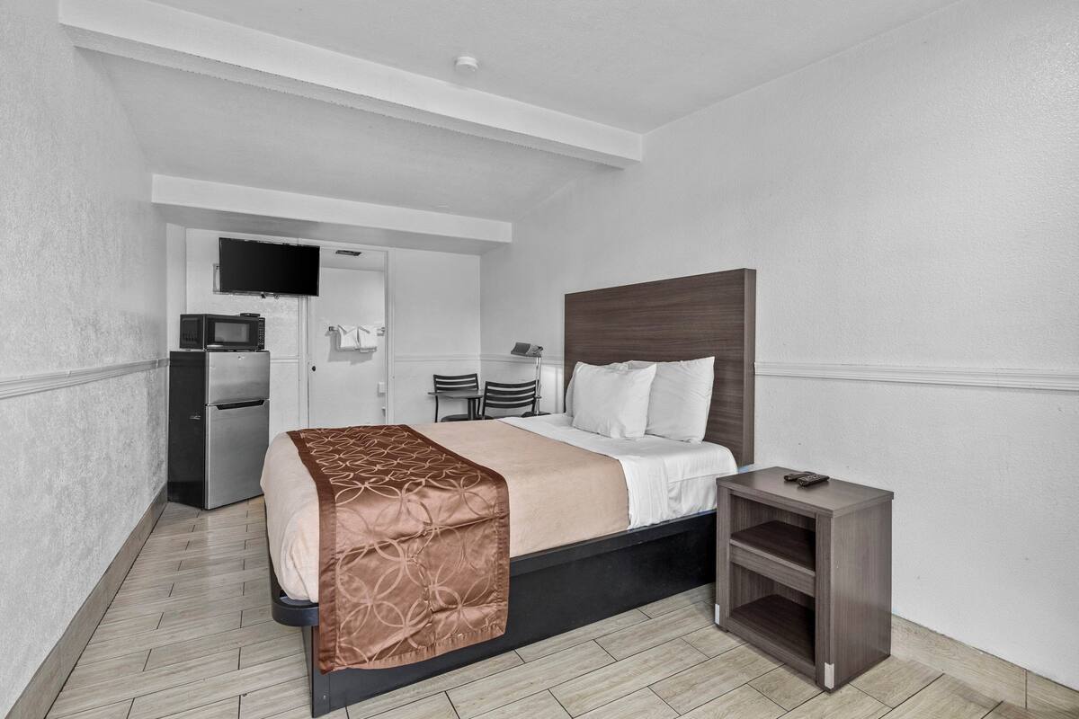 A hotel room with a bed, bedside table, and a small desk with a chair.