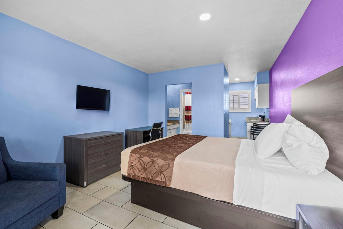 A hotel room with a bed, a desk, a dresser, and a TV on the wall.