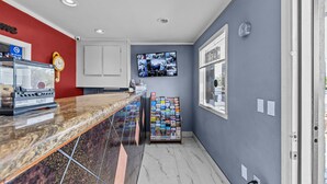 A reception area with a marble counter, a clock, a TV displaying security footage, and a magazine rack. - American Executive Inn (Mesa)