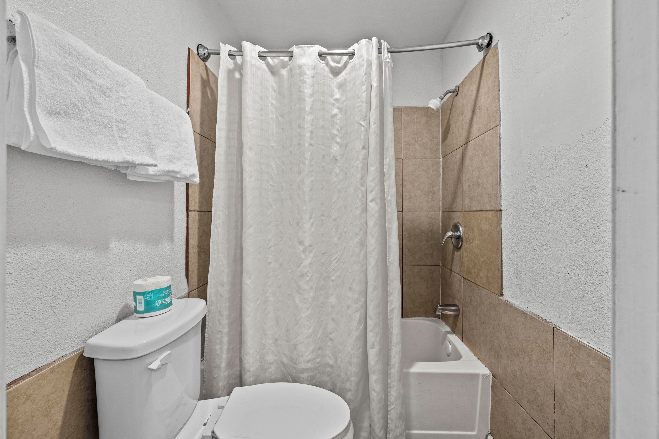 A small, clean bathroom with a toilet, a shower curtain, and a bathtub.