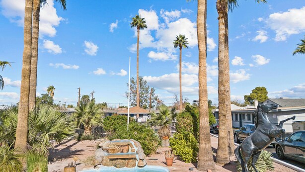 A landscaped area with palm trees, a statue, and a small water feature. - American Executive Inn (Mesa)