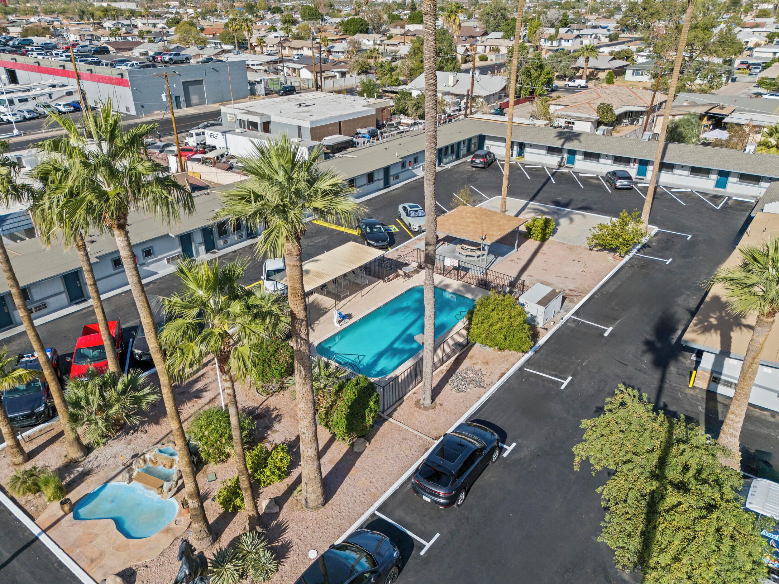 An aerial view of a hotel with a swimming pool, parking lot, and palm trees.