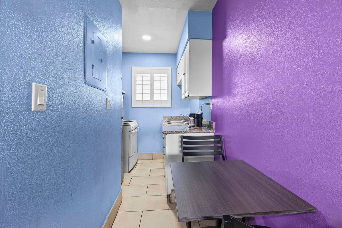 A compact kitchen with blue and purple walls, a small dining table, and basic appliances.