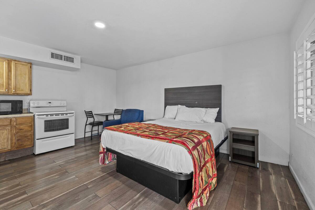 A compact bedroom with a bed, a small desk, and a kitchenette.