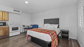 A compact bedroom with a bed, a small desk, and a kitchenette.