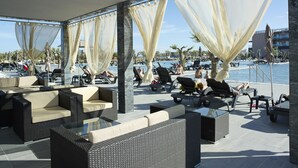 An outdoor lounge area with wicker furniture and sheer curtains, overlooking a pool and water activities. - Vila Gale Lagos Resort Hotel (Lagos)