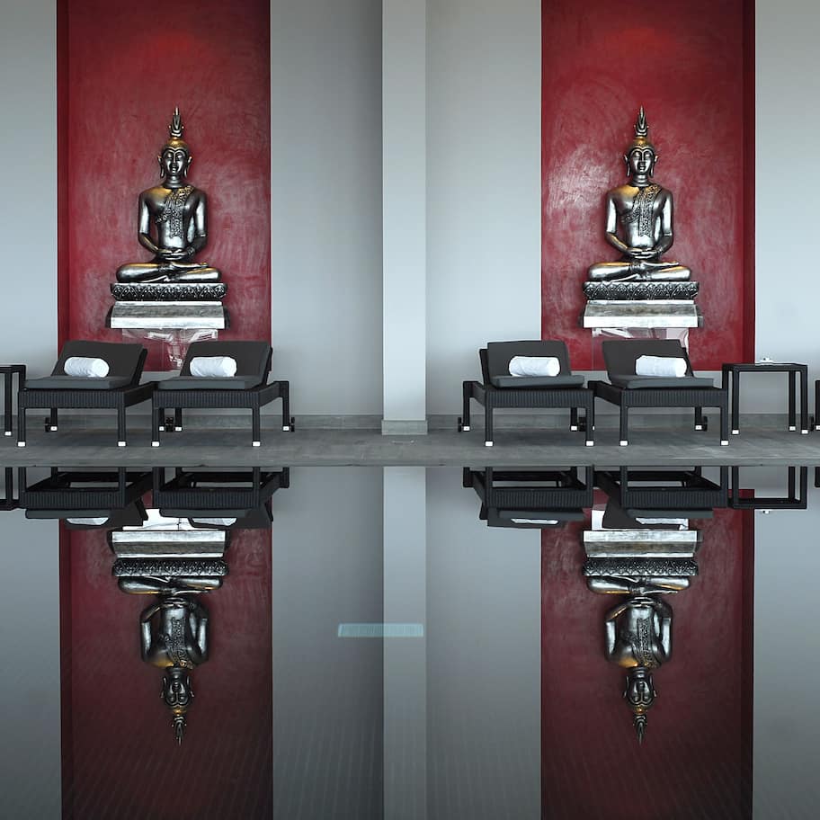 A room with a reflective floor, black lounge chairs, and two large Buddha statues against red walls.
