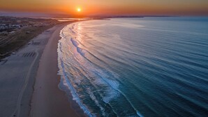 An aerial view of a beach with a sunset, waves, and a distant shoreline. - Vila Gale Lagos Resort Hotel (Lagos)