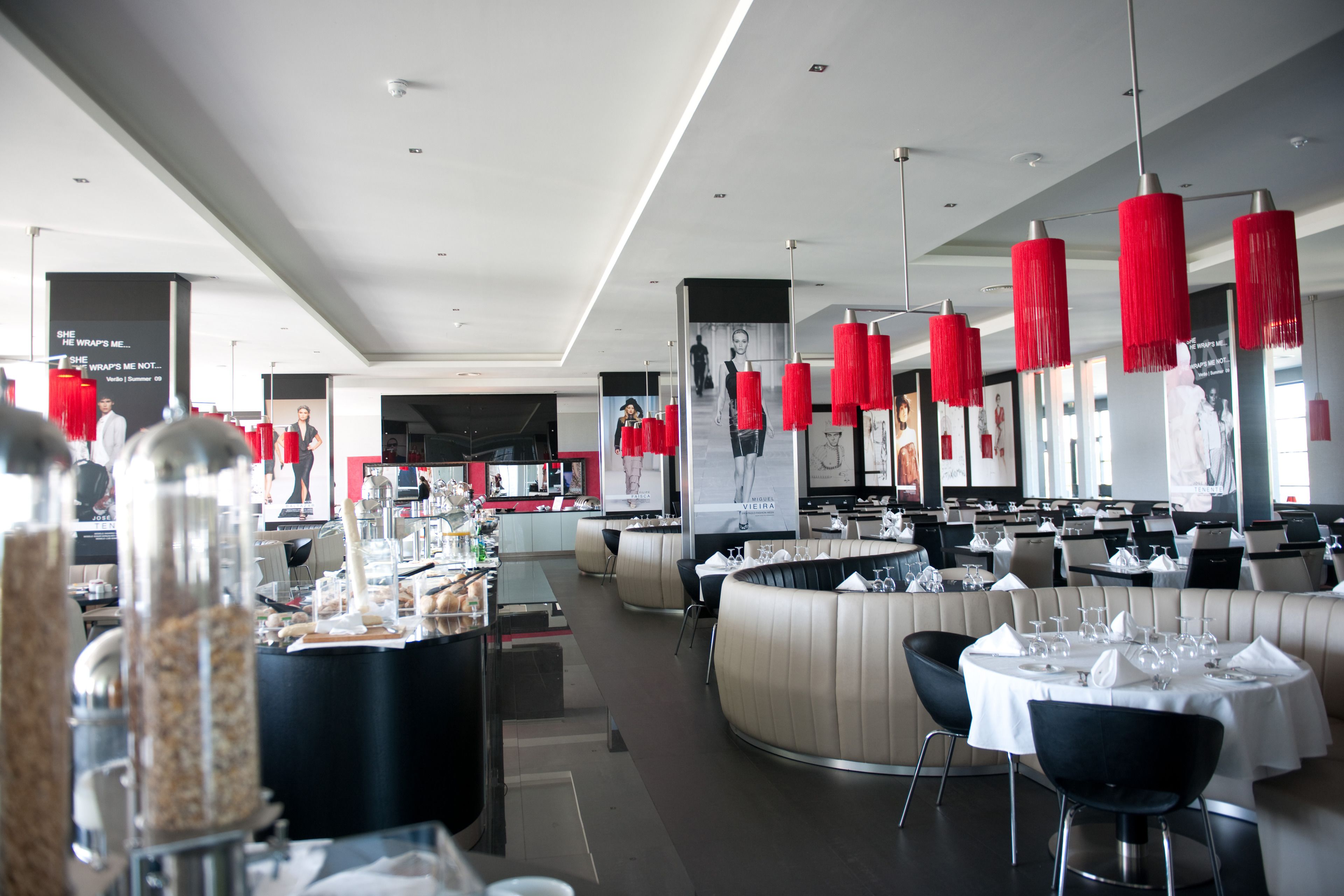 A modern restaurant with round tables, red hanging lights, and a central bar area.