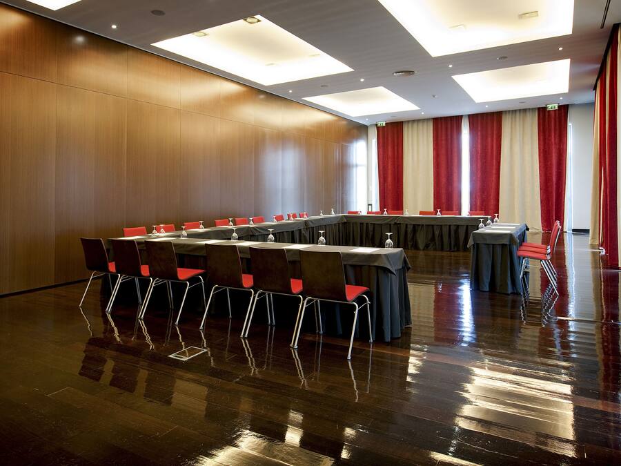 Une salle de conférence avec une longue table, des chaises et un rideau rouge en arrière-plan.