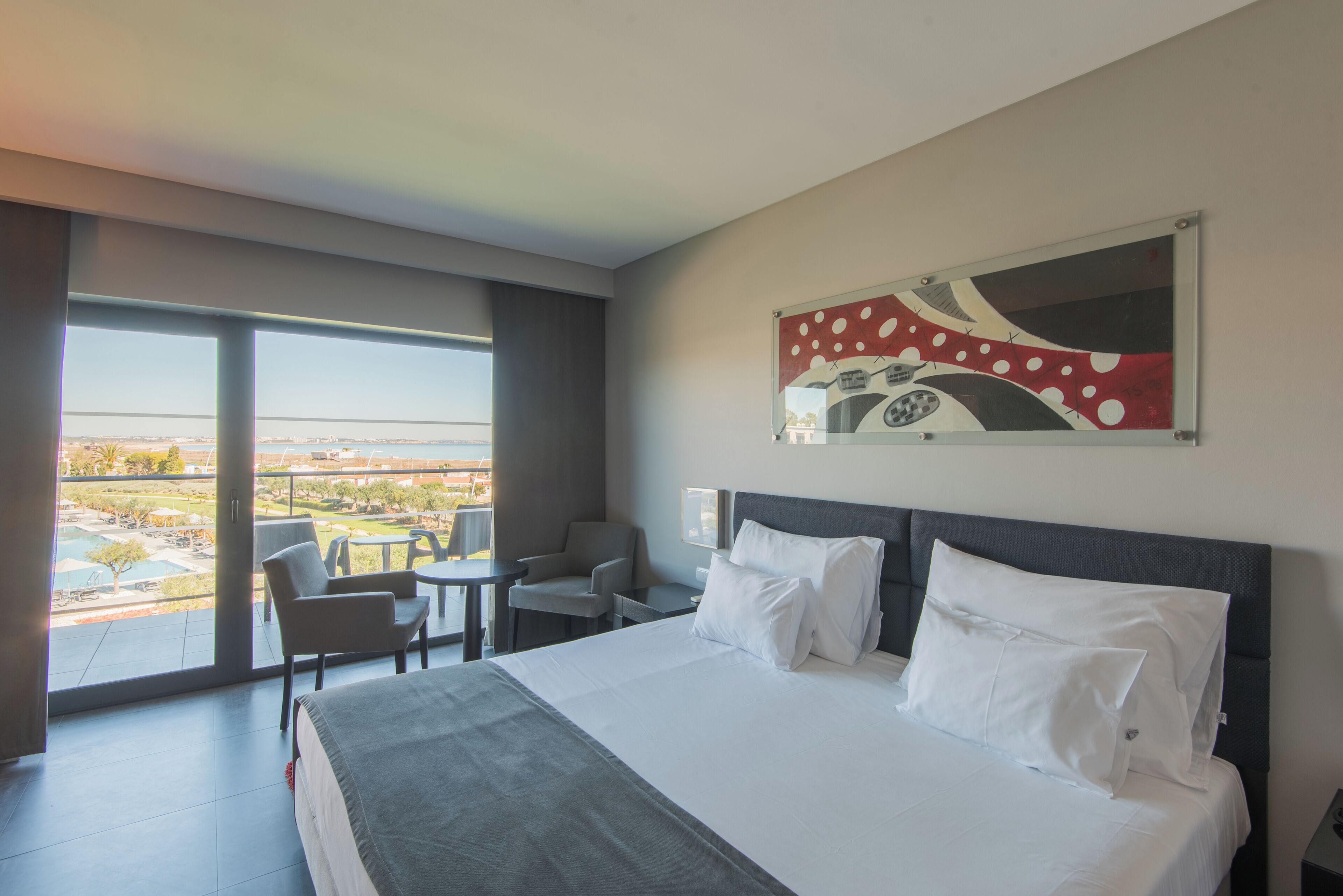 A hotel room with a large bed, a view of the cityscape, and a balcony with seating.