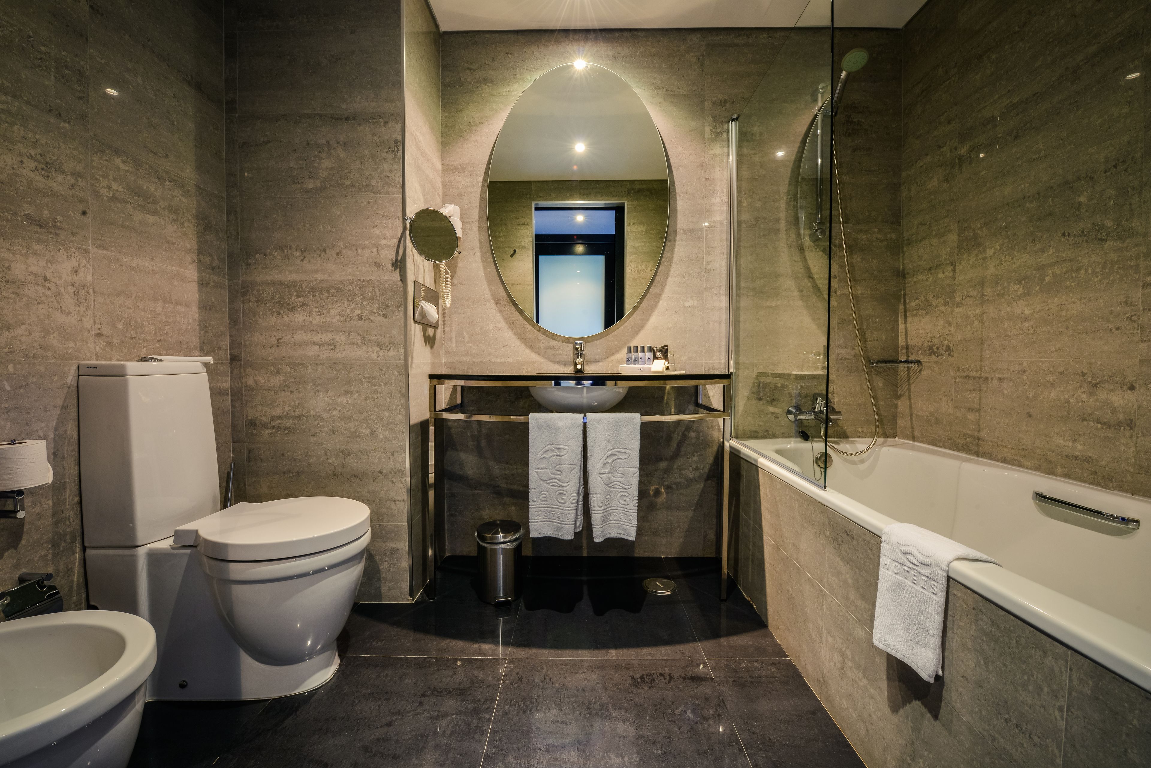 A modern bathroom with a toilet, bidet, sink, and bathtub.