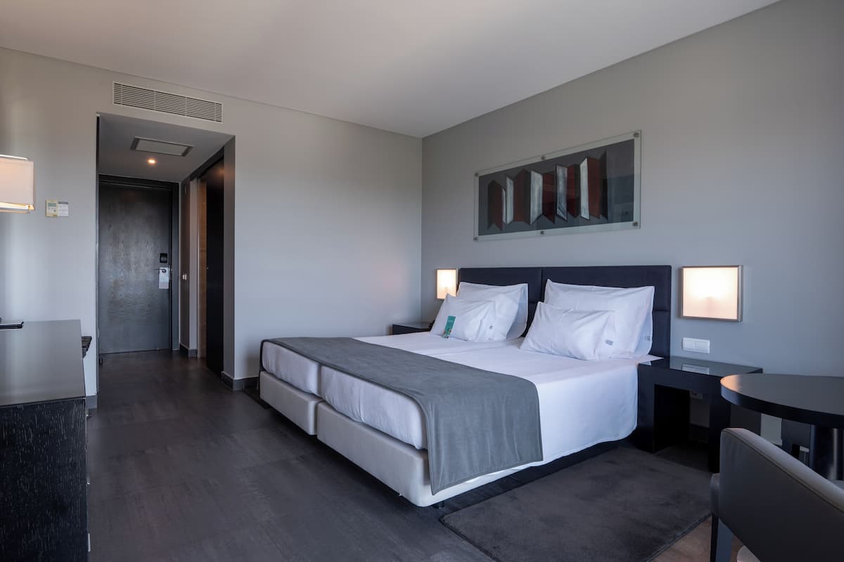 A modern hotel room with a large bed, bedside tables, a desk, and a chair.