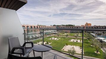 Een balkon met uitzicht op een binnenplaats, met een zwembad, buitenzitplaatsen en een modern gebouw op de achtergrond.