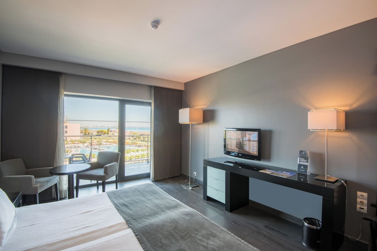 A hotel room with a bed, desk, TV, and seating area.