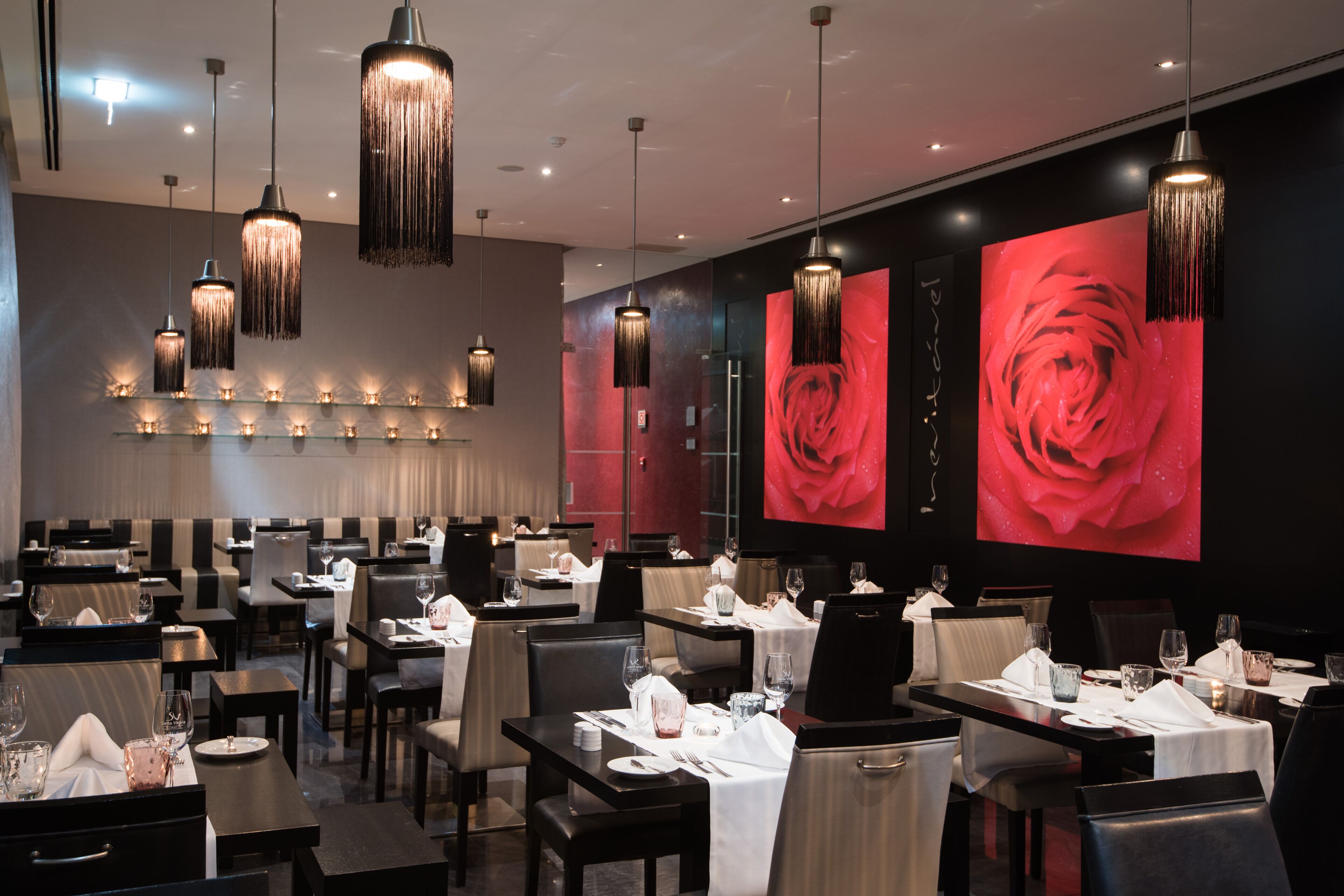 A modern restaurant with multiple dining tables, black and white striped booths, and hanging pendant lights.