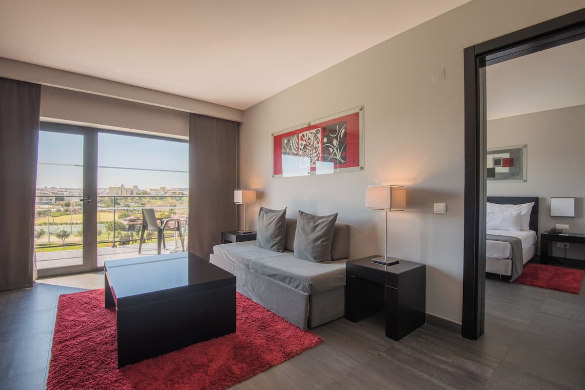 A modern hotel room with a balcony, a bed, a desk, and a red rug.