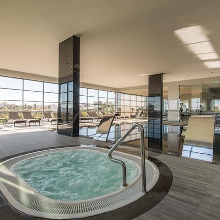 A modern indoor pool area with a hot tub, sunlit seating, and a city view.