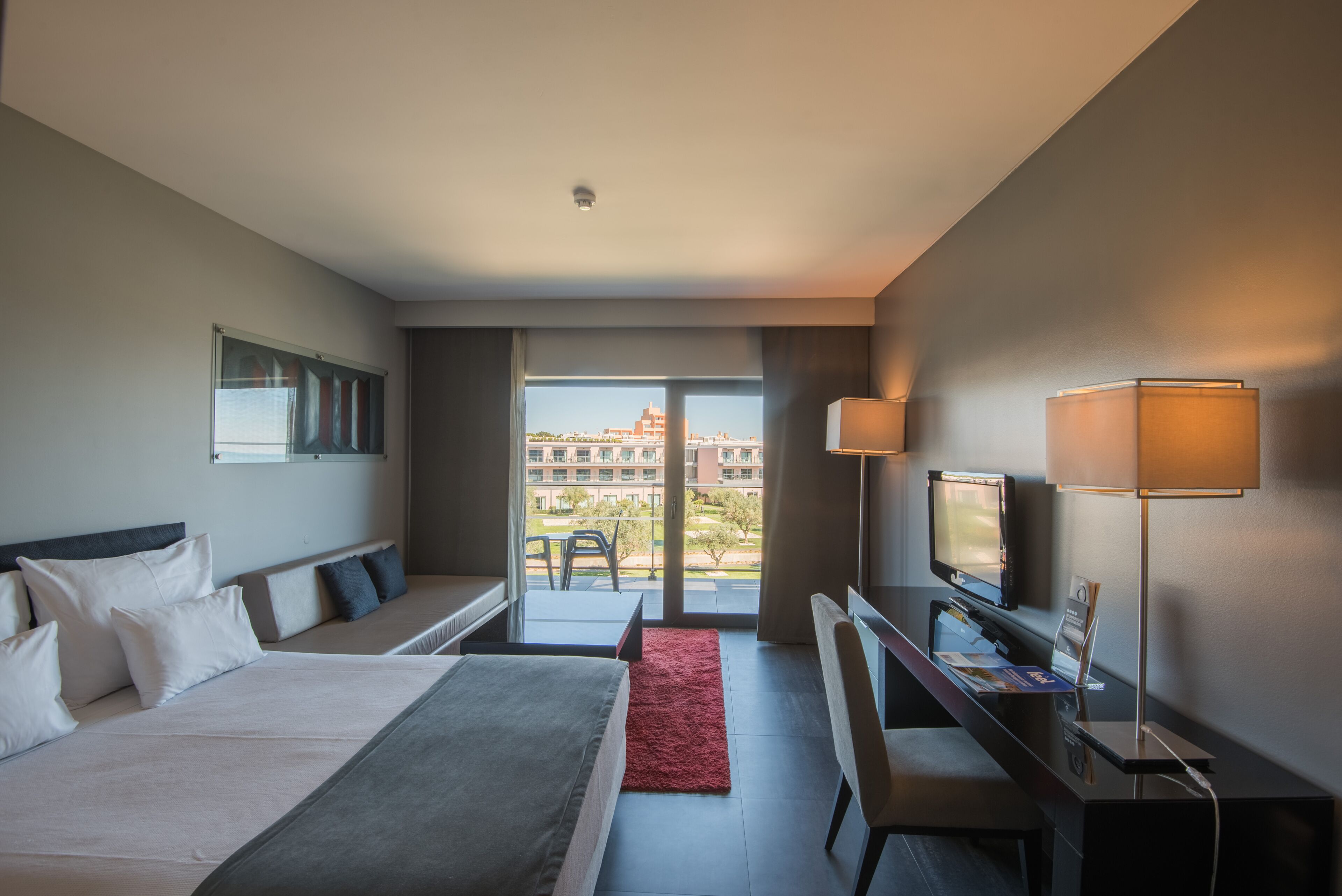 Una camera d'albergo moderna con un letto grande, una scrivania, una televisione e un balcone con vista sulla città.