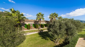 Una villa de estilo mediterráneo con techo de tejas, rodeada de abundante vegetación y palmeras.