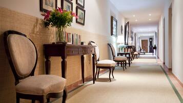 A hotel hallway with a carpeted floor, wooden furniture, and framed pictures on the walls.