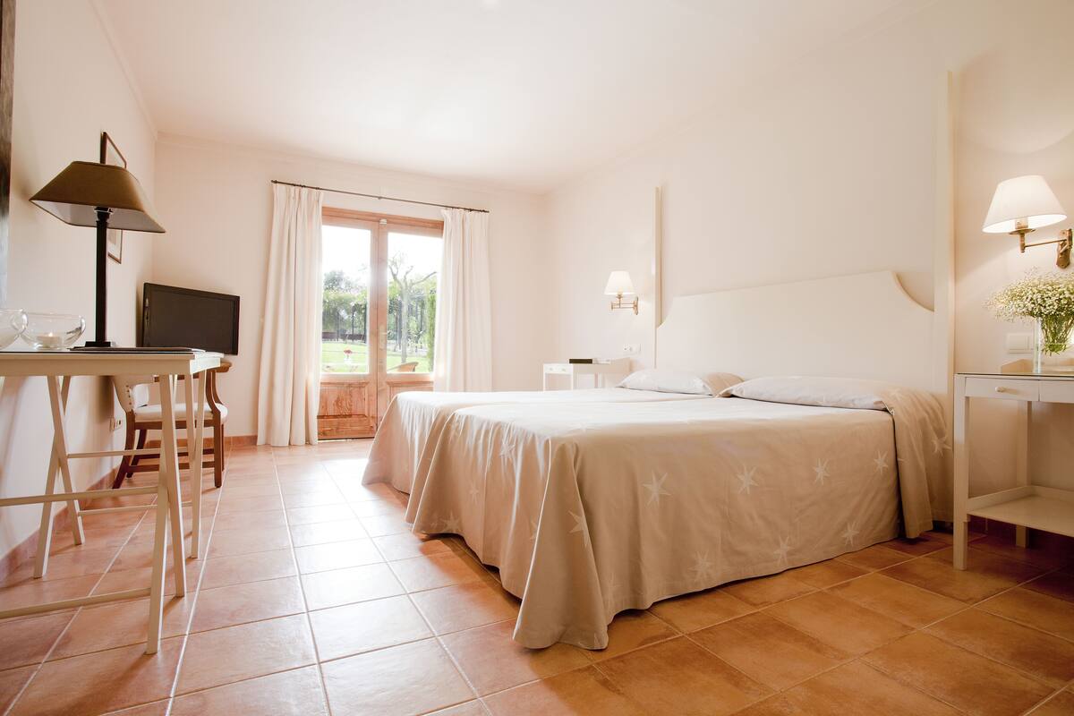 Un dormitorio con cama, escritorio, silla, televisor y ventana con cortinas.