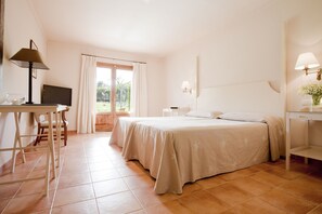 Un dormitorio con cama, escritorio, silla, televisor y ventana con cortinas.