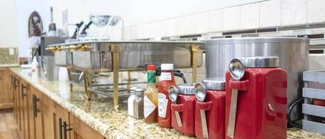 Una encimera de cocina con dispensadores de condimentos, un lavamanos de acero inoxidable y un televisor montado en la pared.