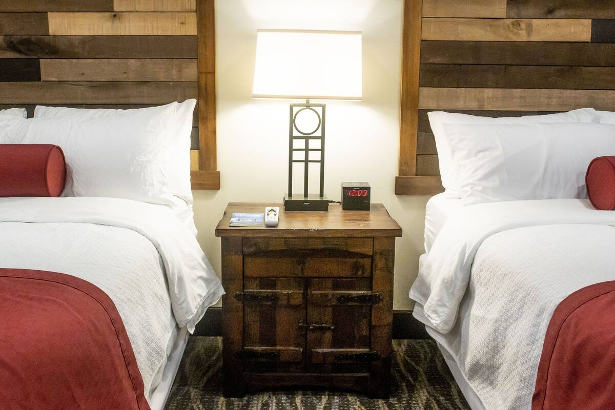 A hotel room with two beds, a nightstand with a lamp, and a digital clock.