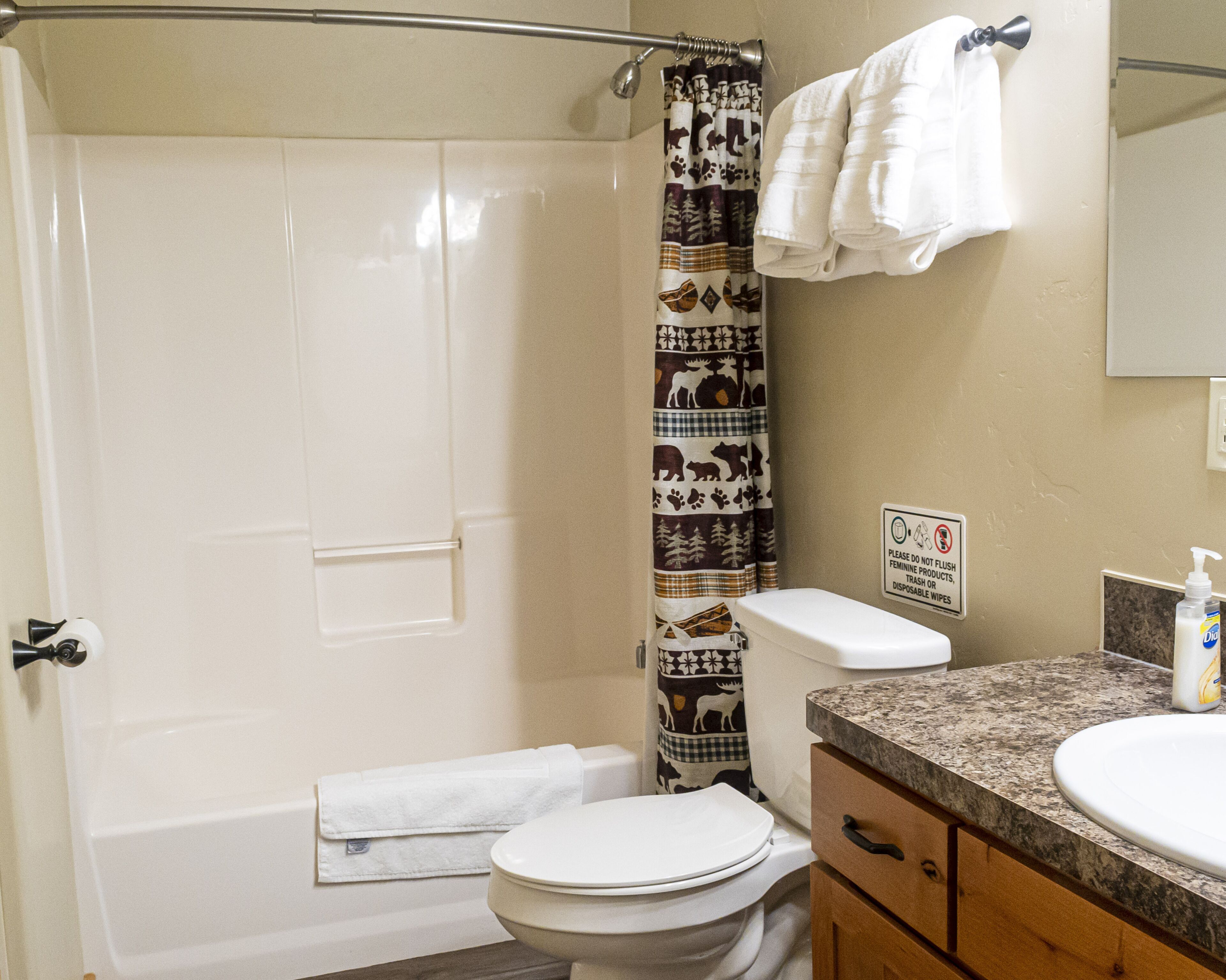 A bathroom with a shower curtain, toilet, sink, and a sign prohibiting flushing feminine products.