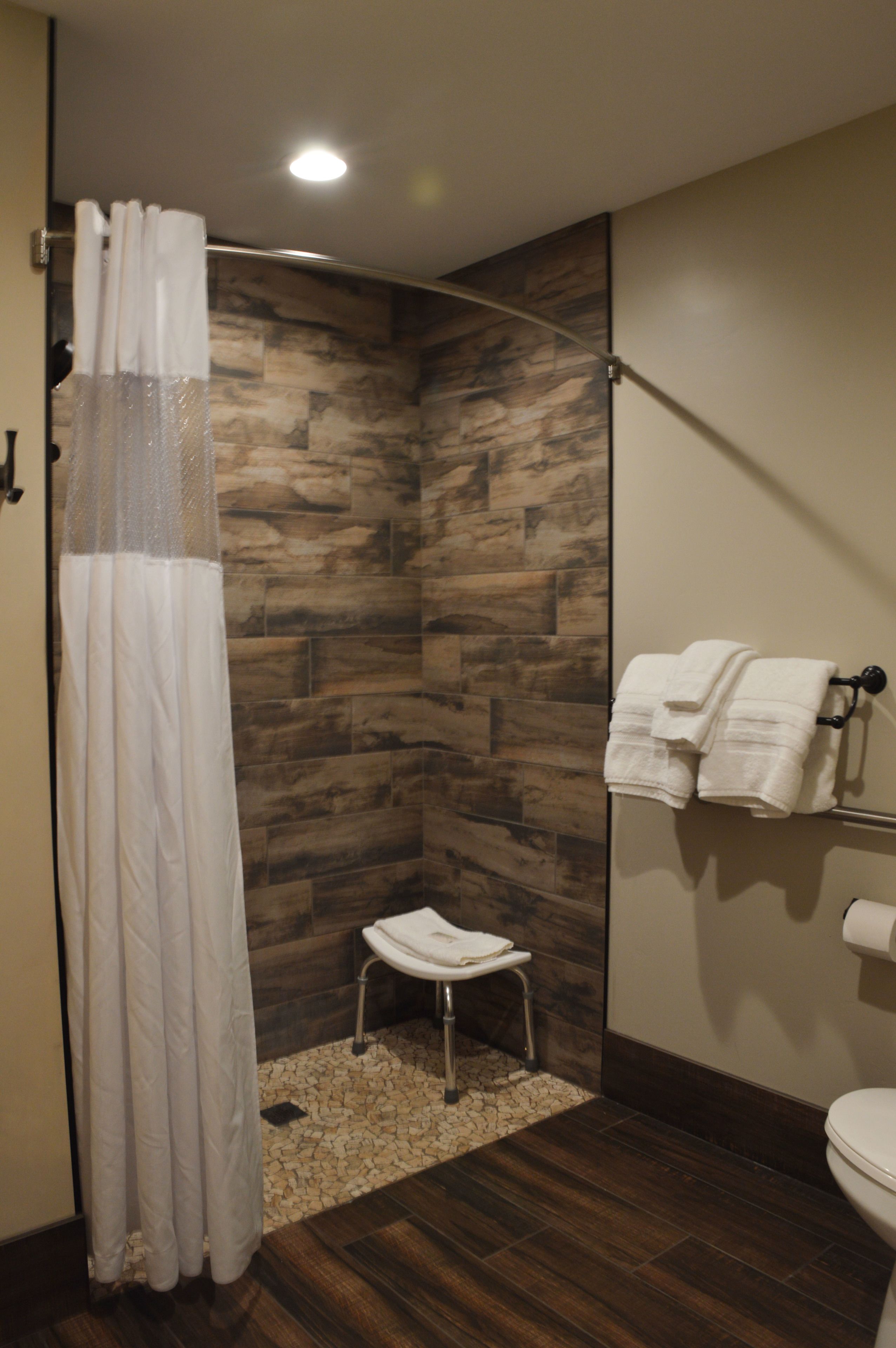 A modern bathroom with a shower, a small stool, and a towel rack.