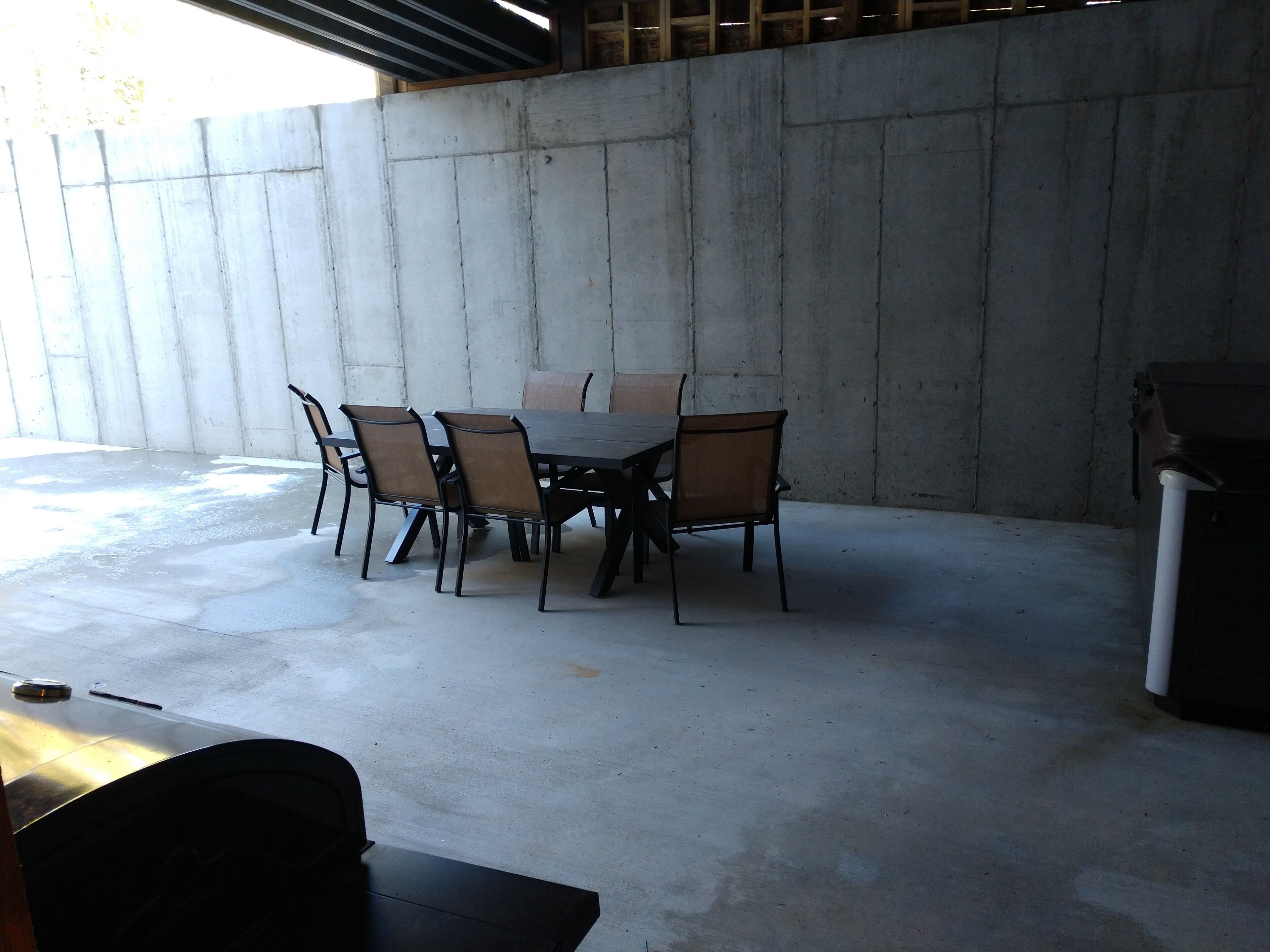 An outdoor patio with a concrete table and chairs, a concrete wall, and a metal trash can.