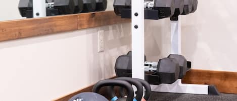 A gym with a mirrored wall, a wooden floor, and exercise equipment including kettlebells, dumbbells, and a medicine ball.