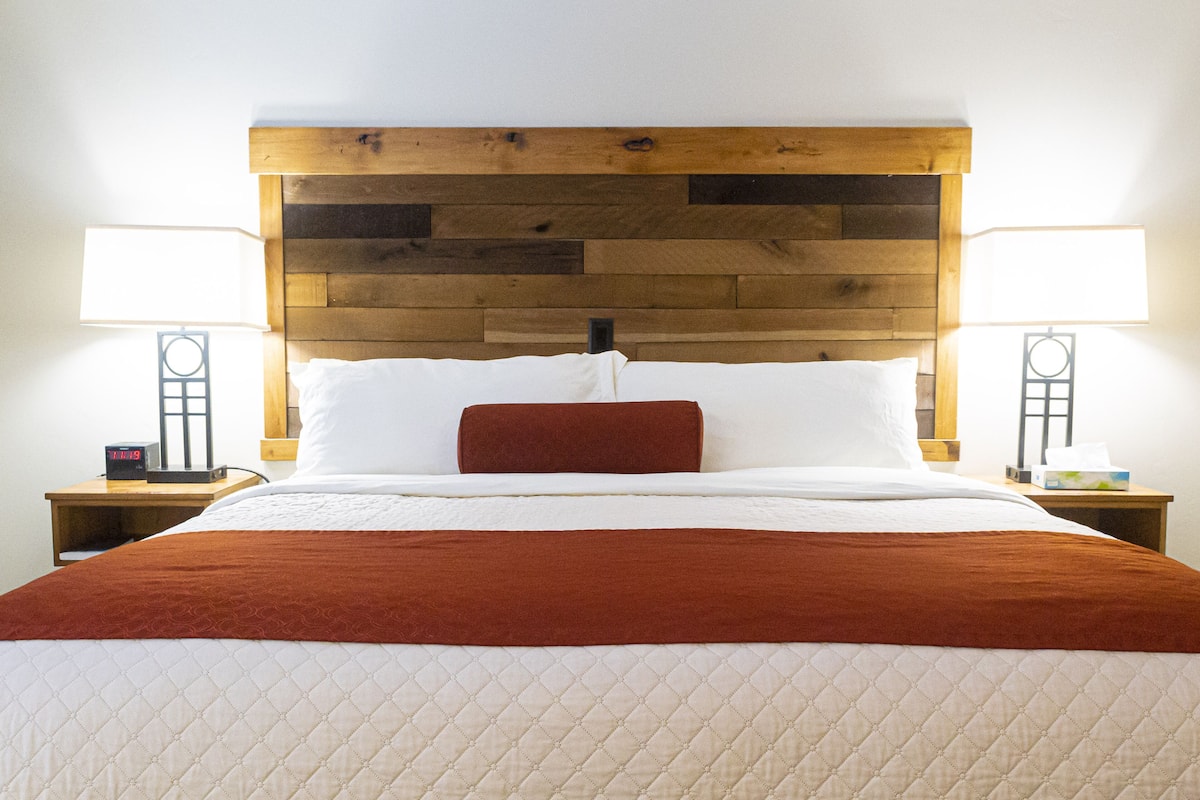 A neatly made bed with a wooden headboard, two bedside lamps, and a red throw blanket.