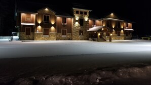 Un edificio grande de varios pisos con fachada de piedra y detalles de madera, con varias ventanas iluminadas y una entrada central con escaleras.