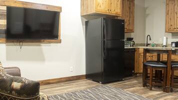 A compact kitchen with wooden cabinets, a black refrigerator, a built-in oven, a coffee maker, and a small dining area with stools.