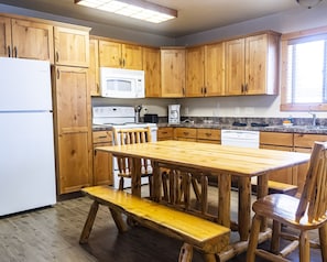 A kitchen with wooden cabinets, a white refrigerator, a microwave, a stove, and a wooden dining table with benches.