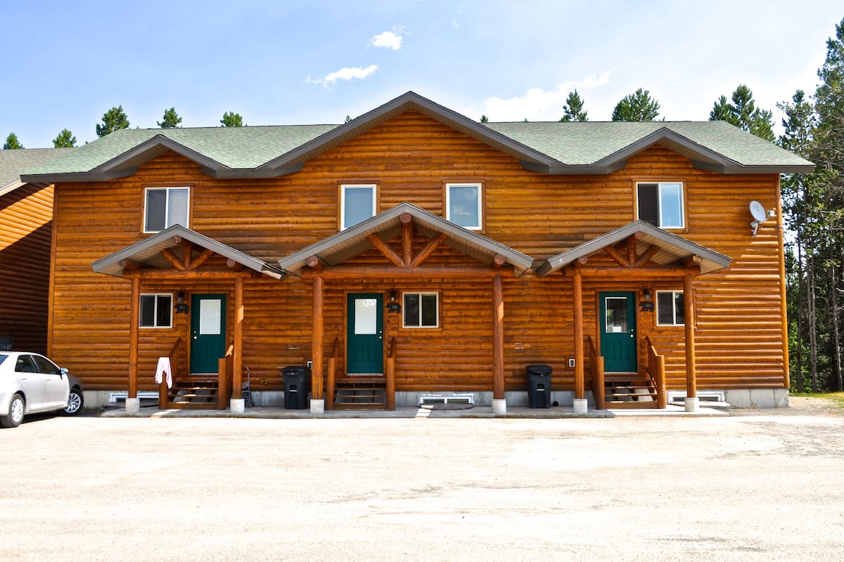 A log cabin with a front porch, two windows, and a green door.