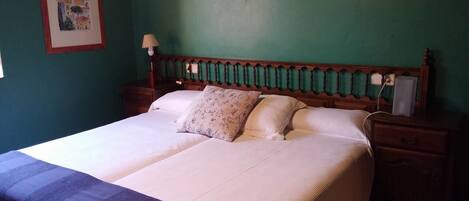 A double bed with a white and blue striped bedspread, two pillows, a wooden headboard, a bedside table with a lamp, and a framed picture on the wall.