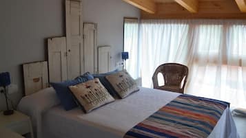 Een slaapkamer met een groot bed, een stoel en een raam met dunne gordijnen.