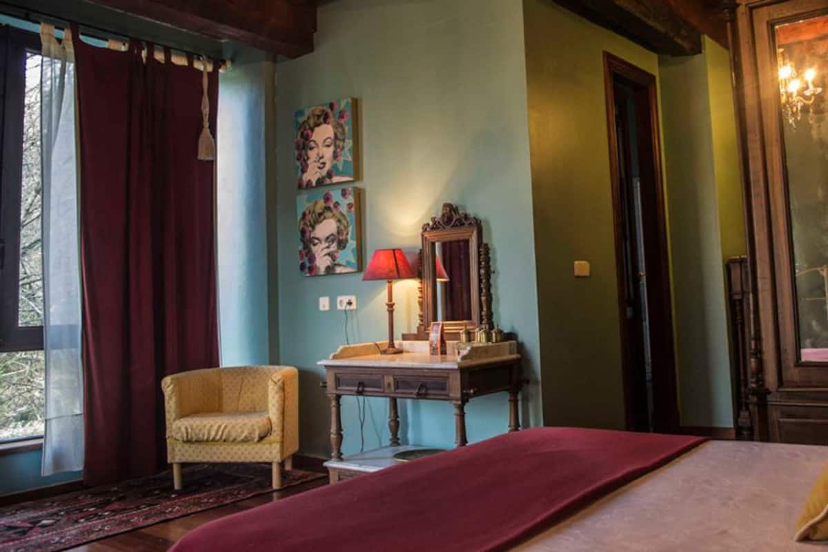 A bedroom with a bed, a chair, a desk, and a mirror.