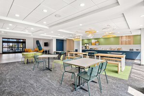 A modern, well-lit indoor space with multiple tables and chairs, a reception area, and a view through large windows. - Spark by Hilton Lancaster Dutch Country (Lancaster)